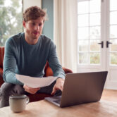 Man Sitting On Armchair At Home With Laptop Paying Bill Online