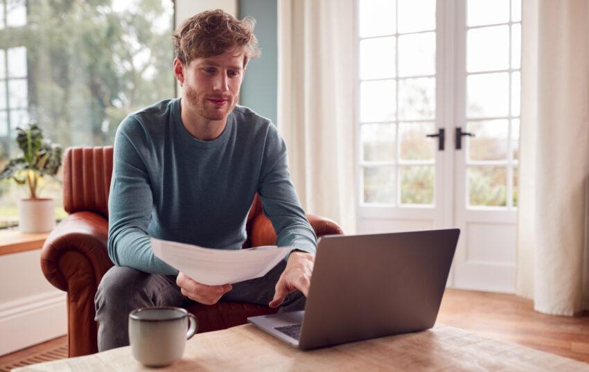 Man Sitting On Armchair At Home With Laptop Paying Bill Online