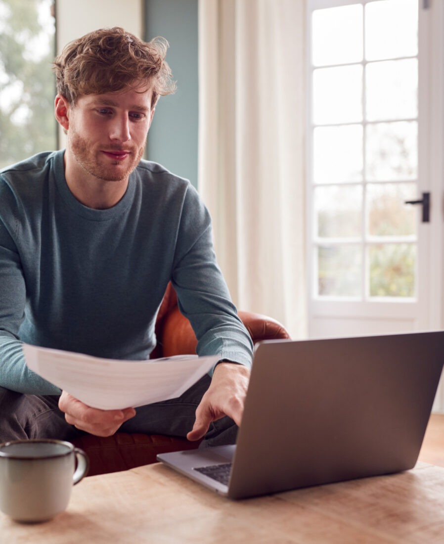 Man Sitting On Armchair At Home With Laptop Paying Bill Online